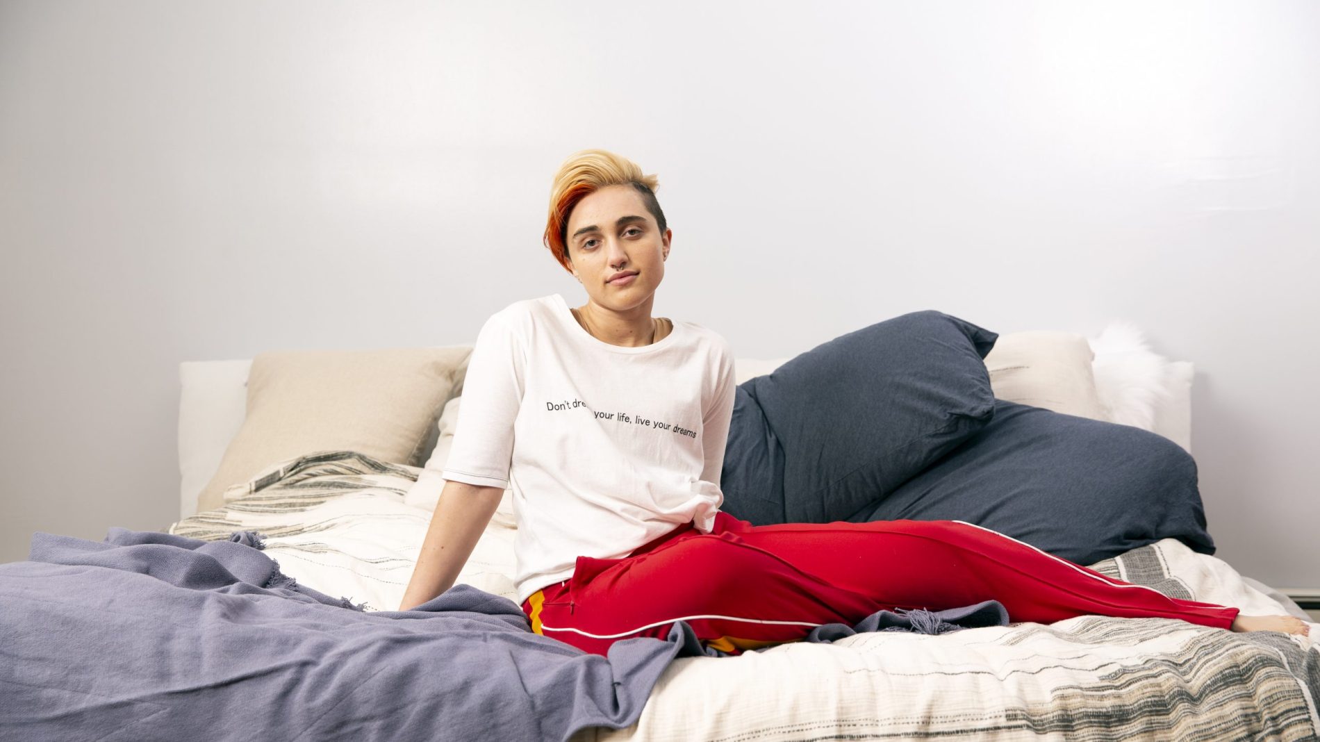 A trans young person sitting on a bed