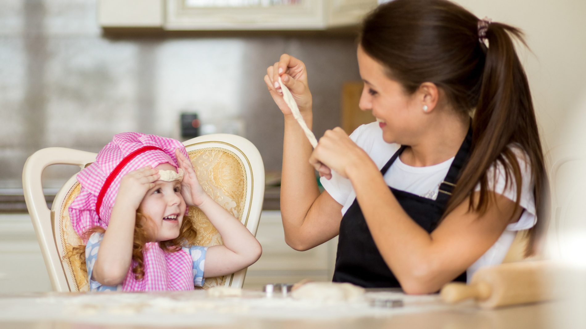 Happy mother and little girl making fun with dough