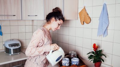 Young woman preparing tea in the kitchen. Pouring water into a cup.