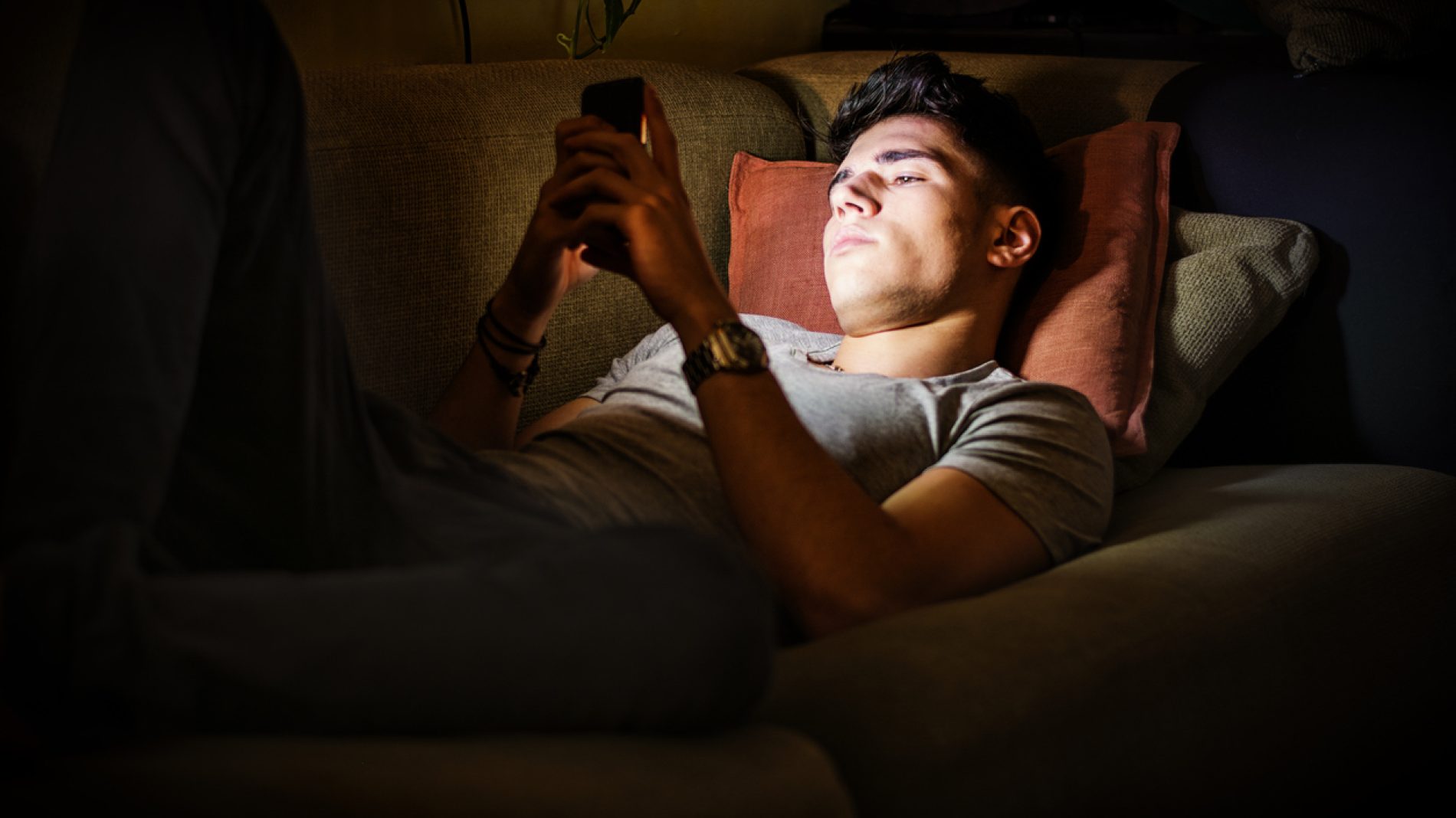 Young Man on Sofa Lit by Light from Cell Phone