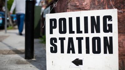 A uk Polling station sign hooked on a wall on a street