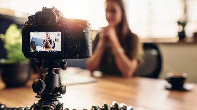 Digital camera on flexible tripod recording a video of woman at desk.