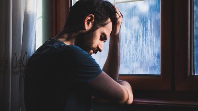 Man leaning against a window looking sad