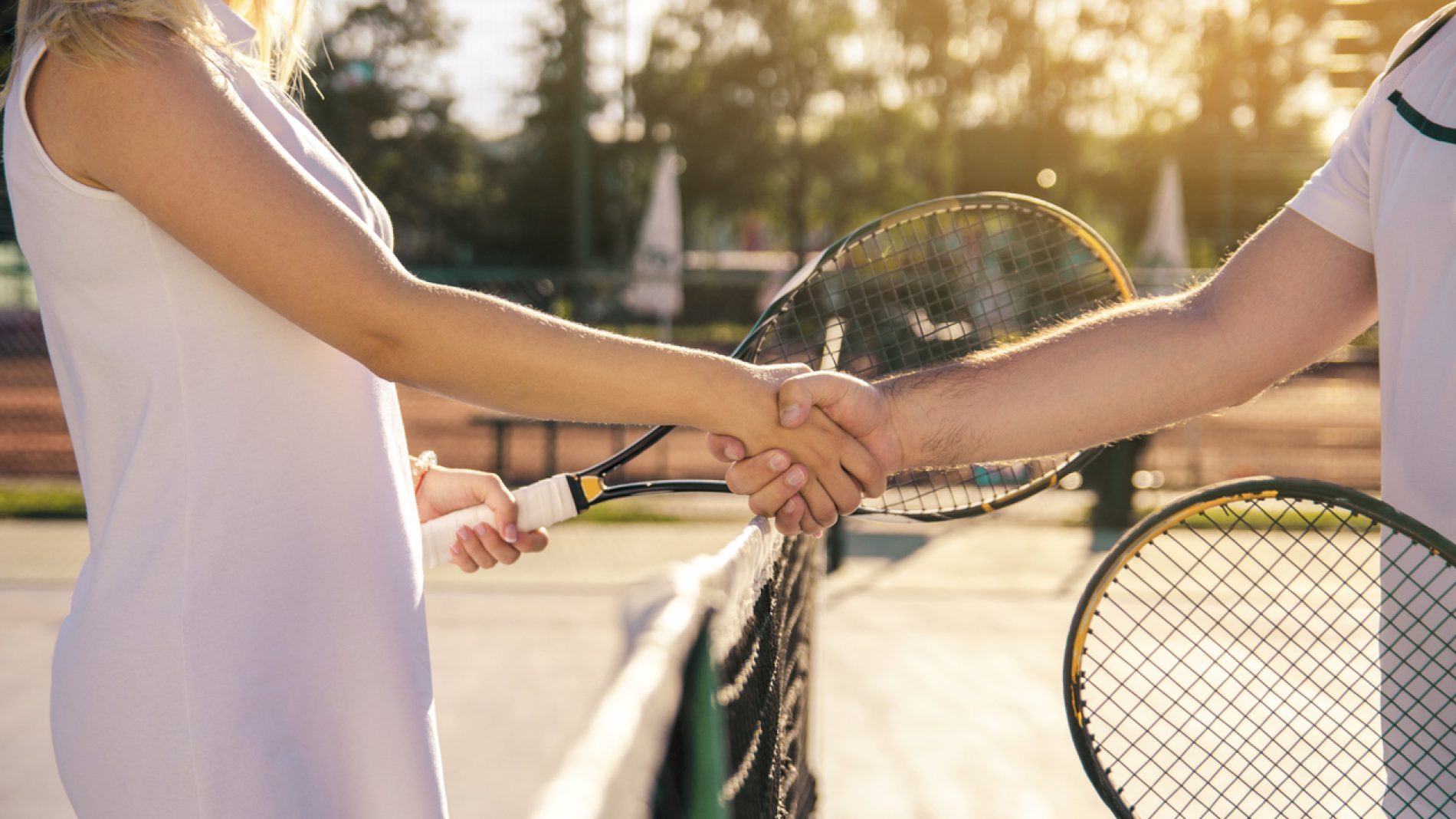 Male and female tennis players shaking hands on net