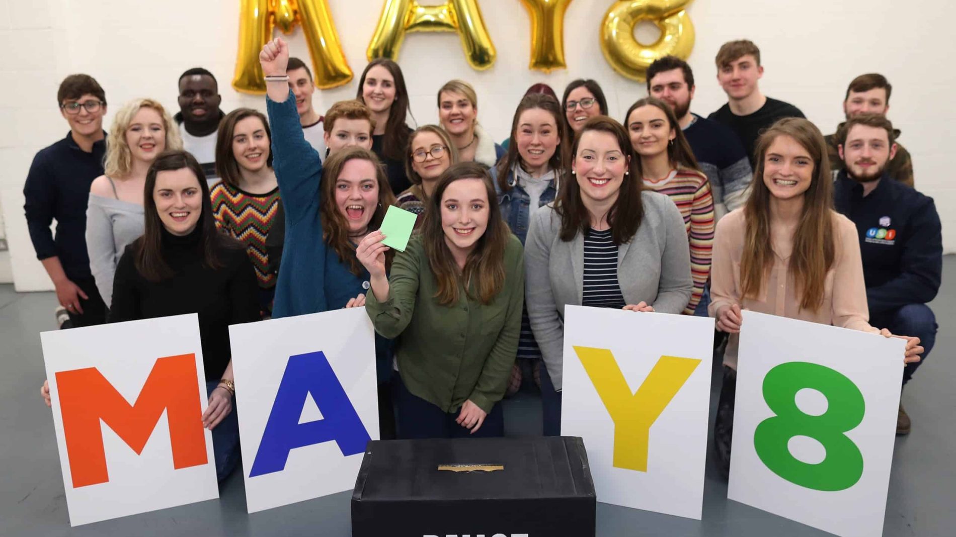 Young people with May 8 signs, in front of a ballot box