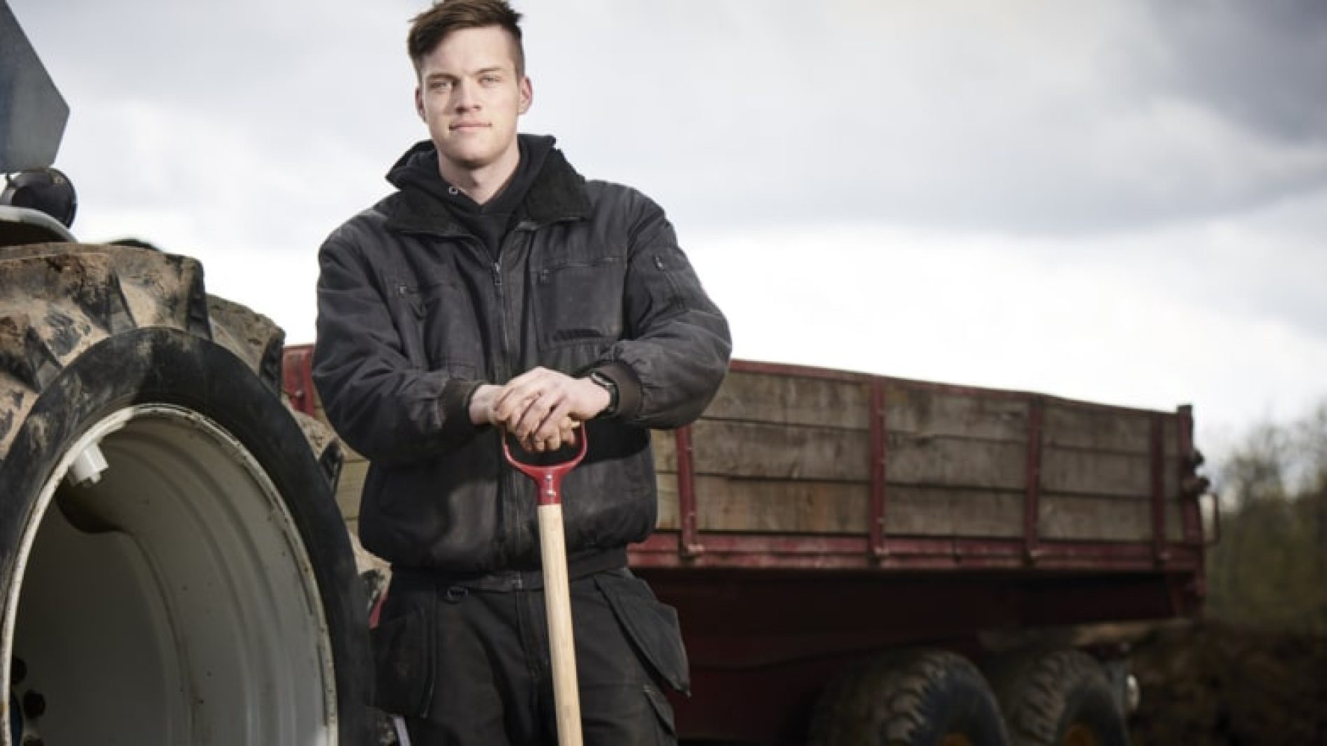 Young-farmer-standing-infront-of-a-tractor-HoEKkq
