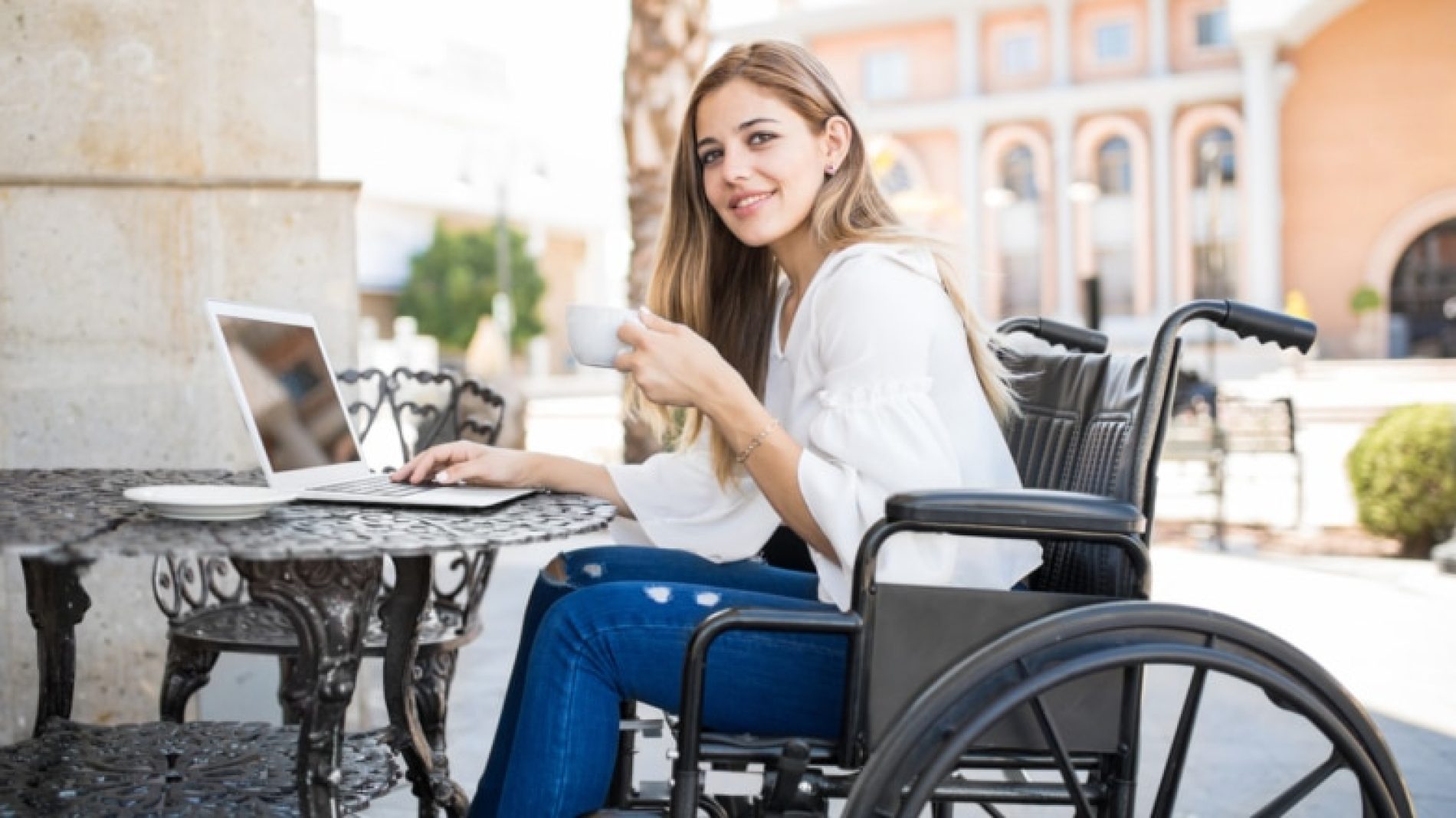 Young-woman-in-wheelchair-drinking-tea-with-laptop-aeKfhP