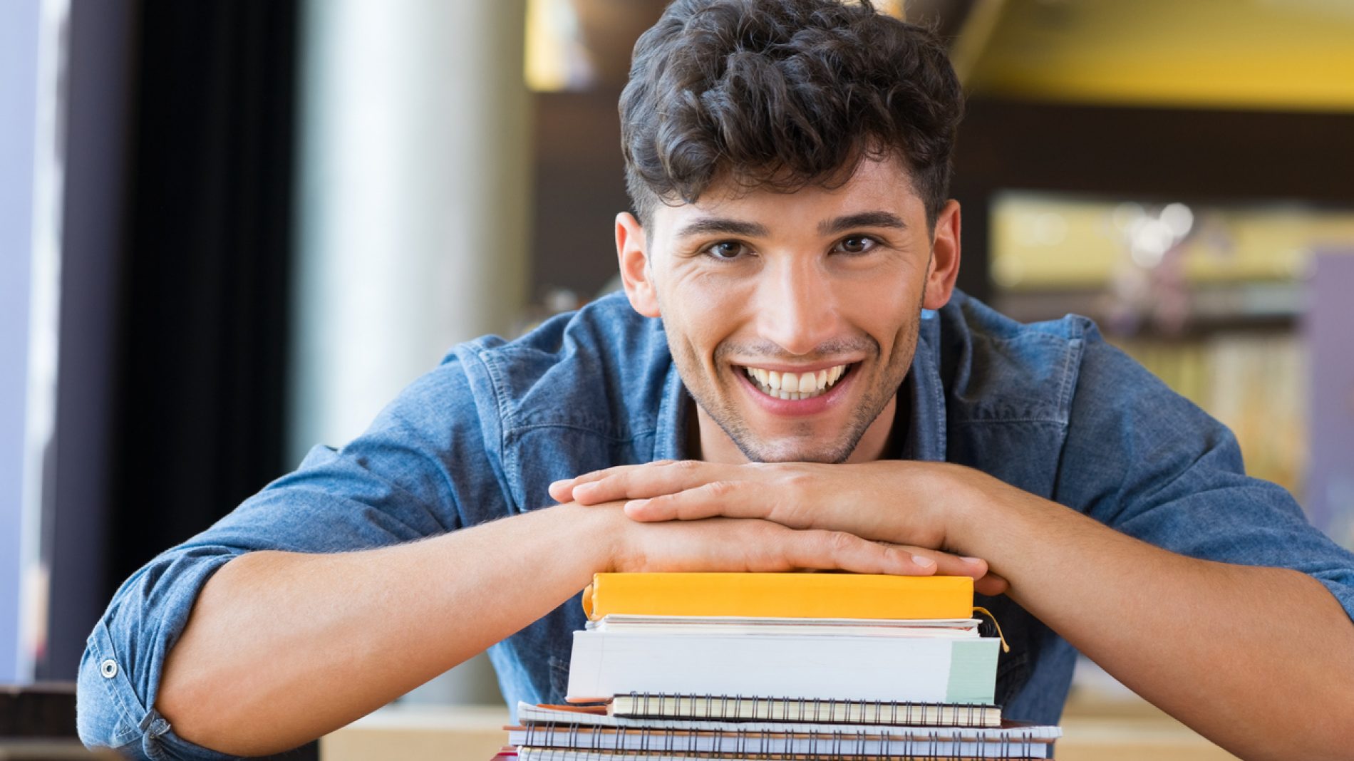 Smiling young man leaning on a stack of books
