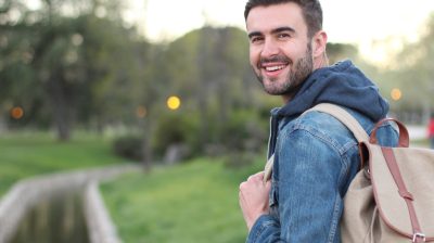 Smiley male holding backpack outdoors with copyspace