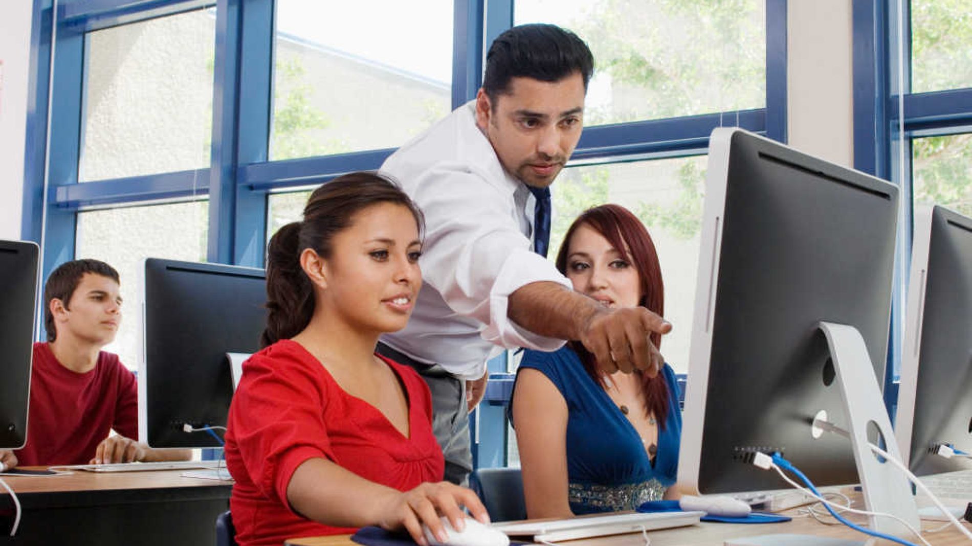 Photo of two people sitting at a computer with a teacher pointing at the screen - VTOS