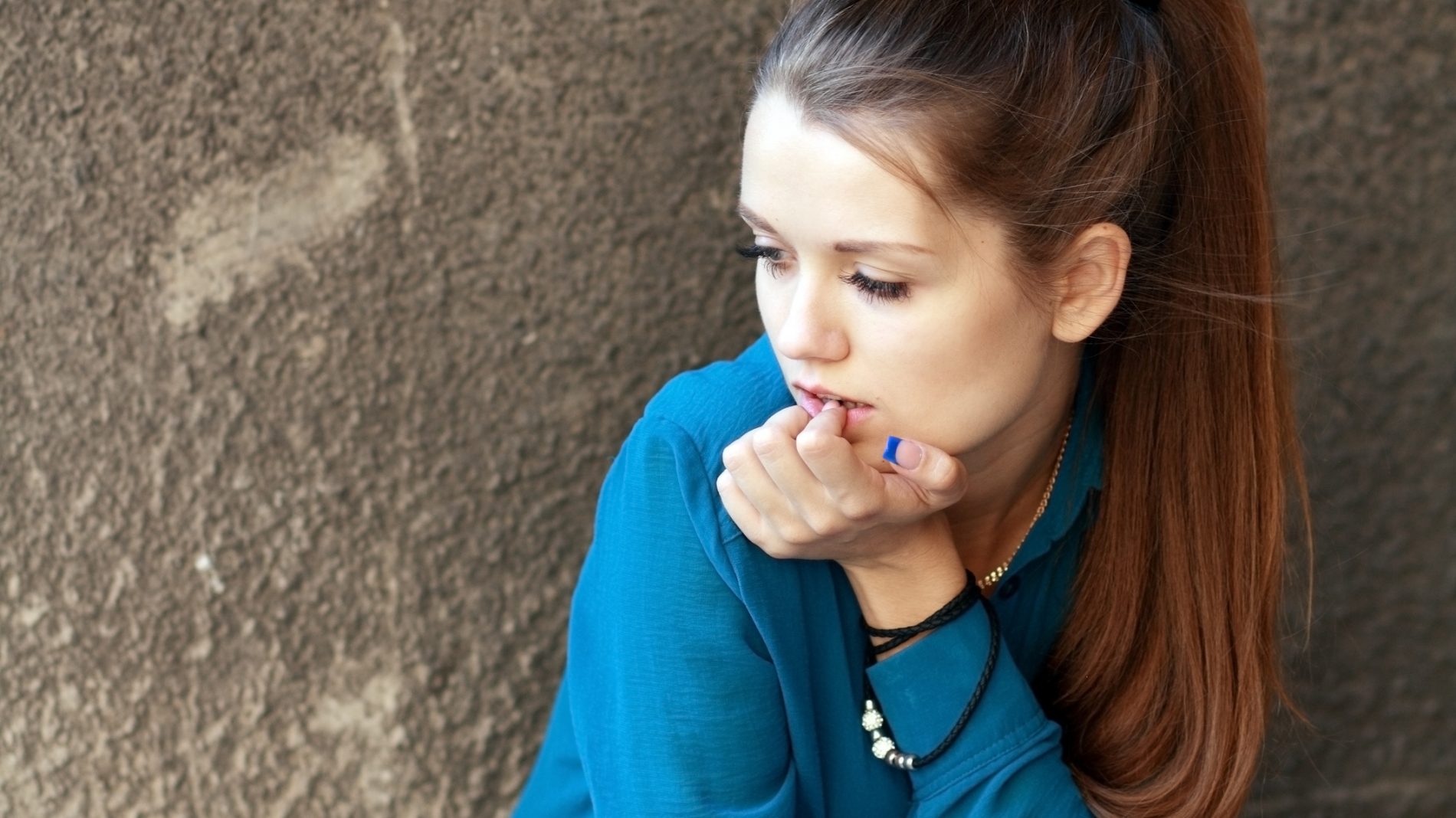A girl in a blue shirt sitting against a concrete wall