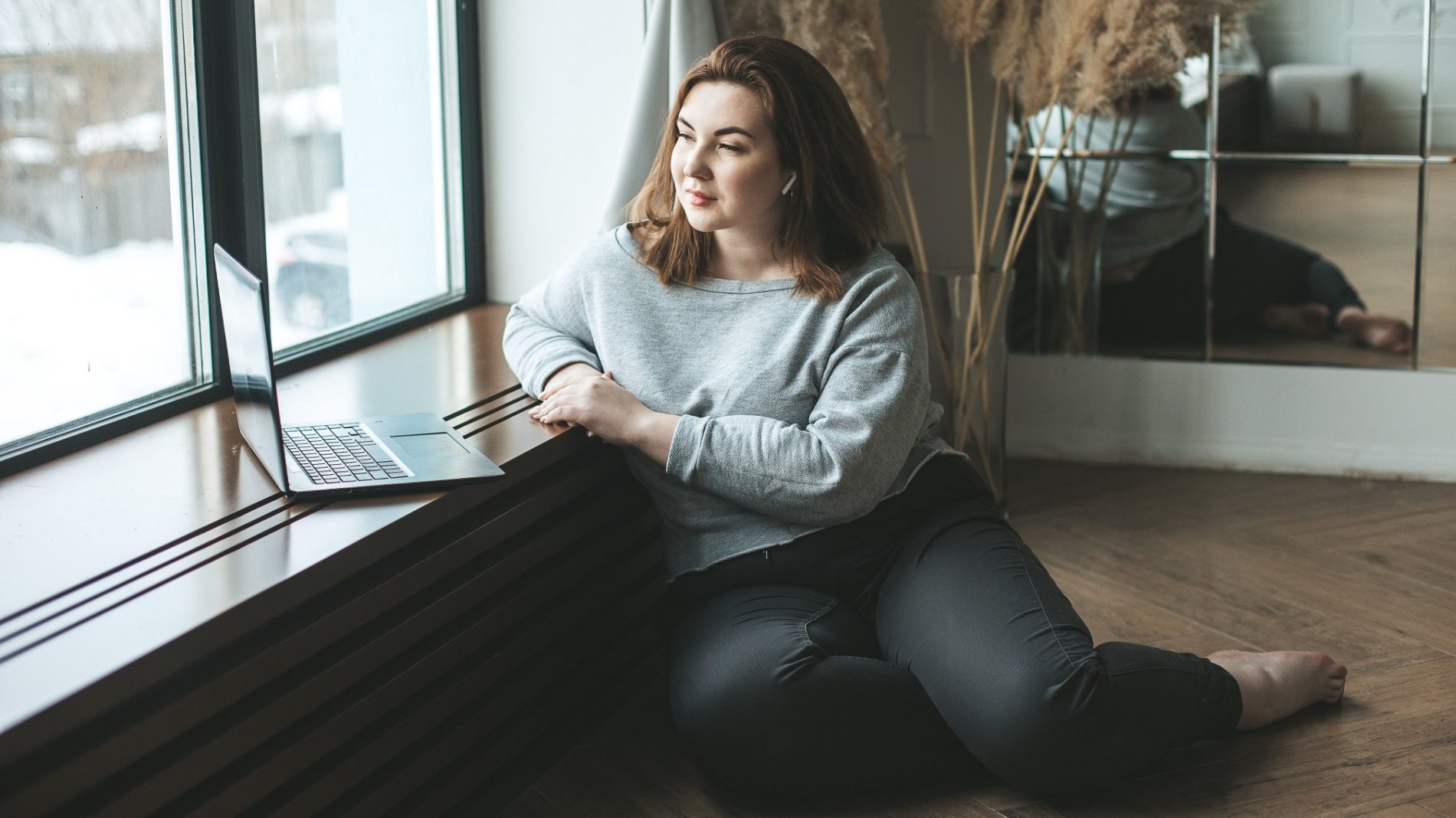 Photo of a person sitting on the floor with their laptop resting on the windowsill - Back to Work Enterprise Allowance
