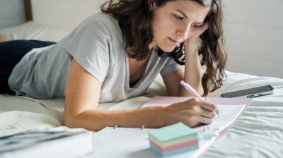 Photo of a person lying on a bed writing in a notebook - balance burnout