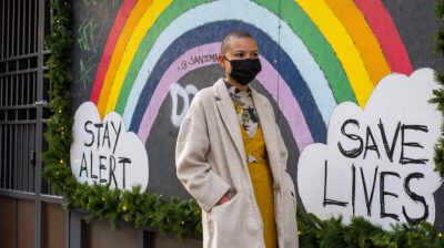 feminine presenting person wearing mask as a precaution against the spread of coronavirus walks past a rainbow sign \ restrictions covid 19 ireland