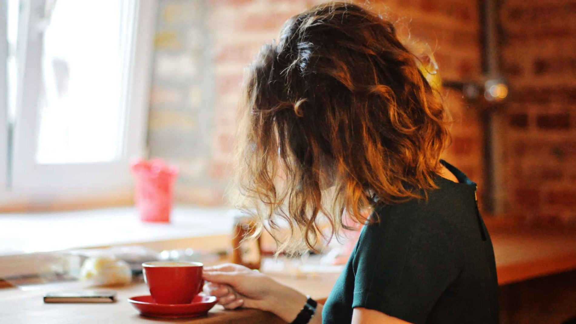 Photo of a young person sitting in a cafe drinking out of a red cup - conviction
