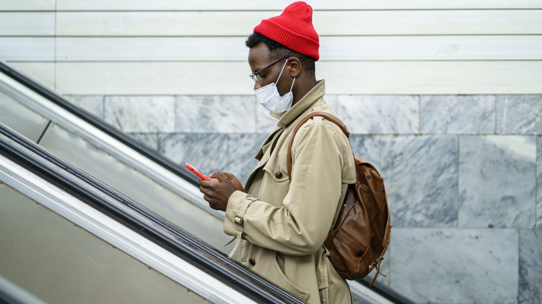 Photo of a person standing on an escalator wearing a face mask and looking at their phone