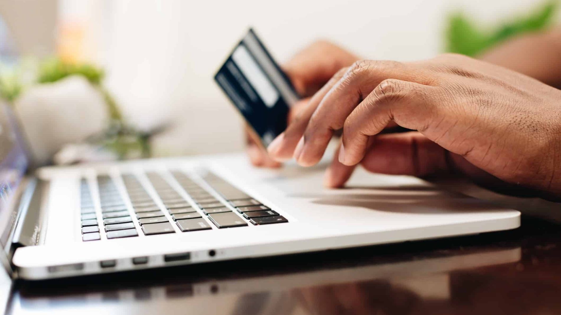 Photo of a person's hands on a laptop with a credit card in one hand