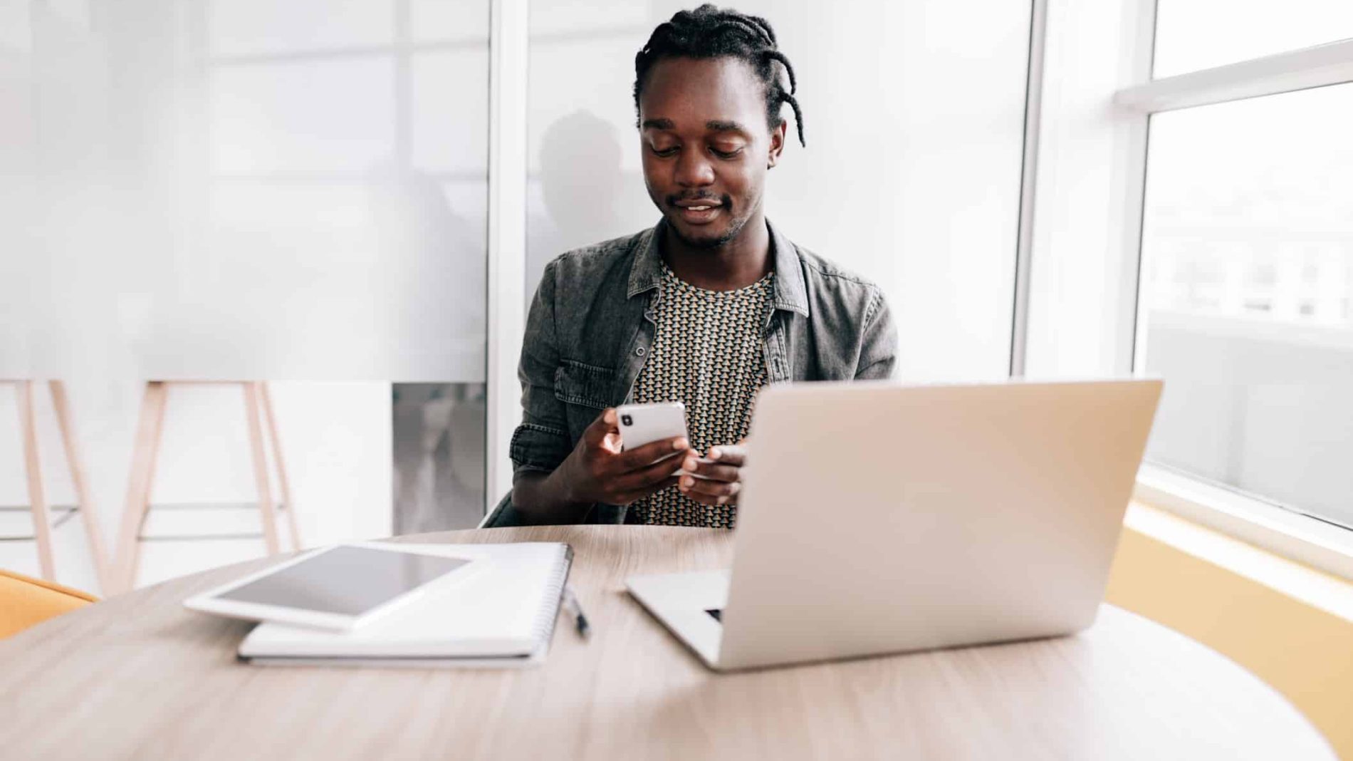 Photo of a person looking at their phone at a desk with a laptop and notebooks