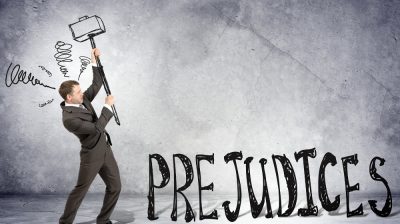 Businessman with hammer and word prejudices on grey wall background