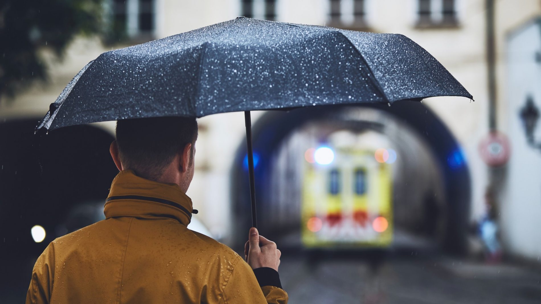 A man standing in the rain with an umbrella looking for emergency accommodation