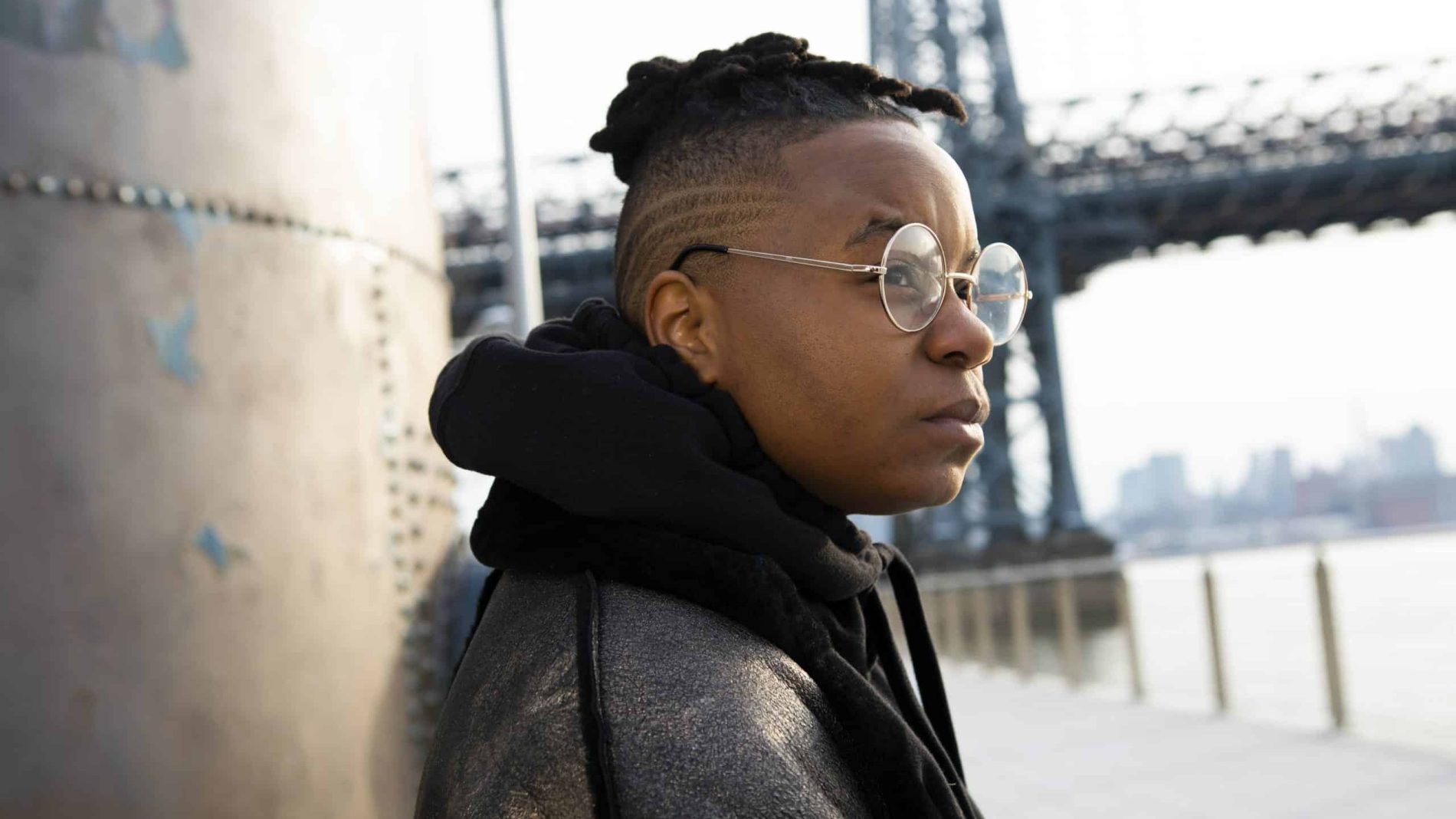 A young person leaning against a wall looking into the distance