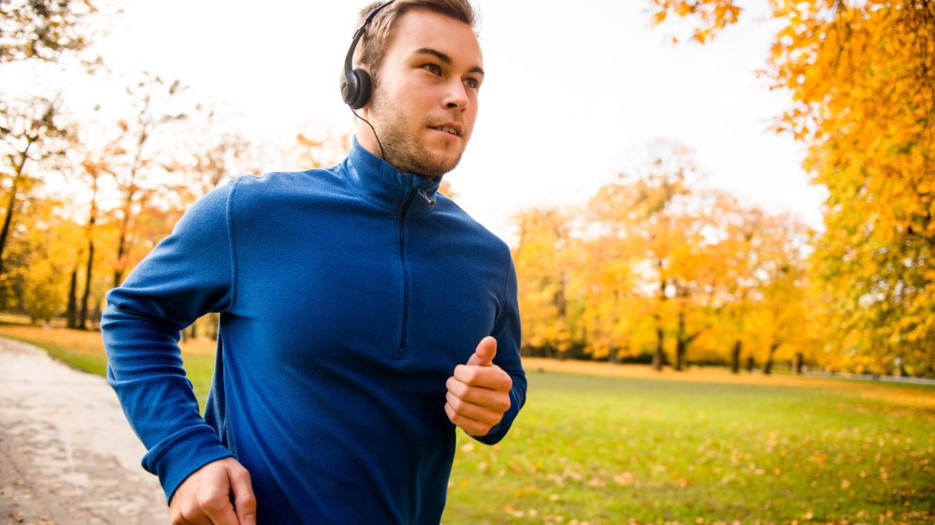 Young man with headphones running in autumn nature and listening music