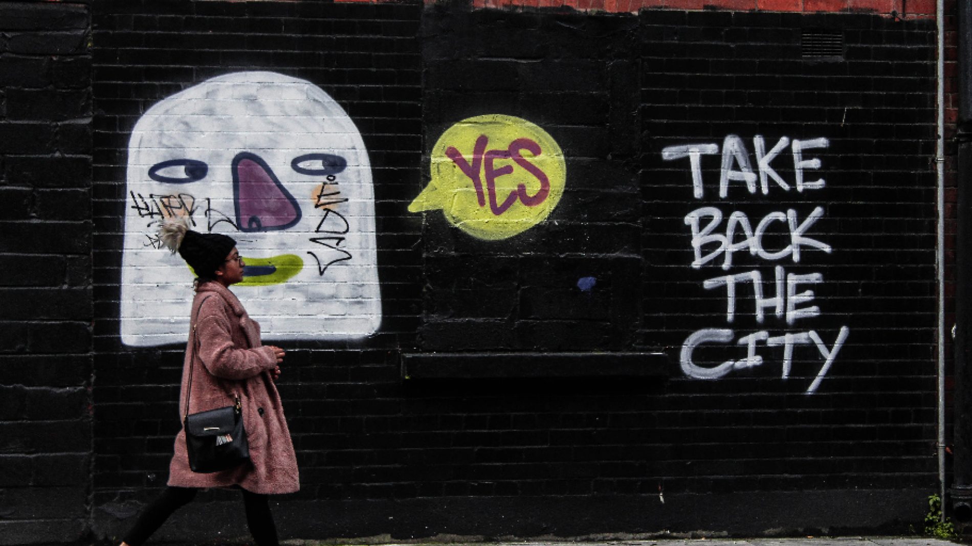 feminine person walking in front of graffiti reading ' take back the city ' - housing crisis ireland
