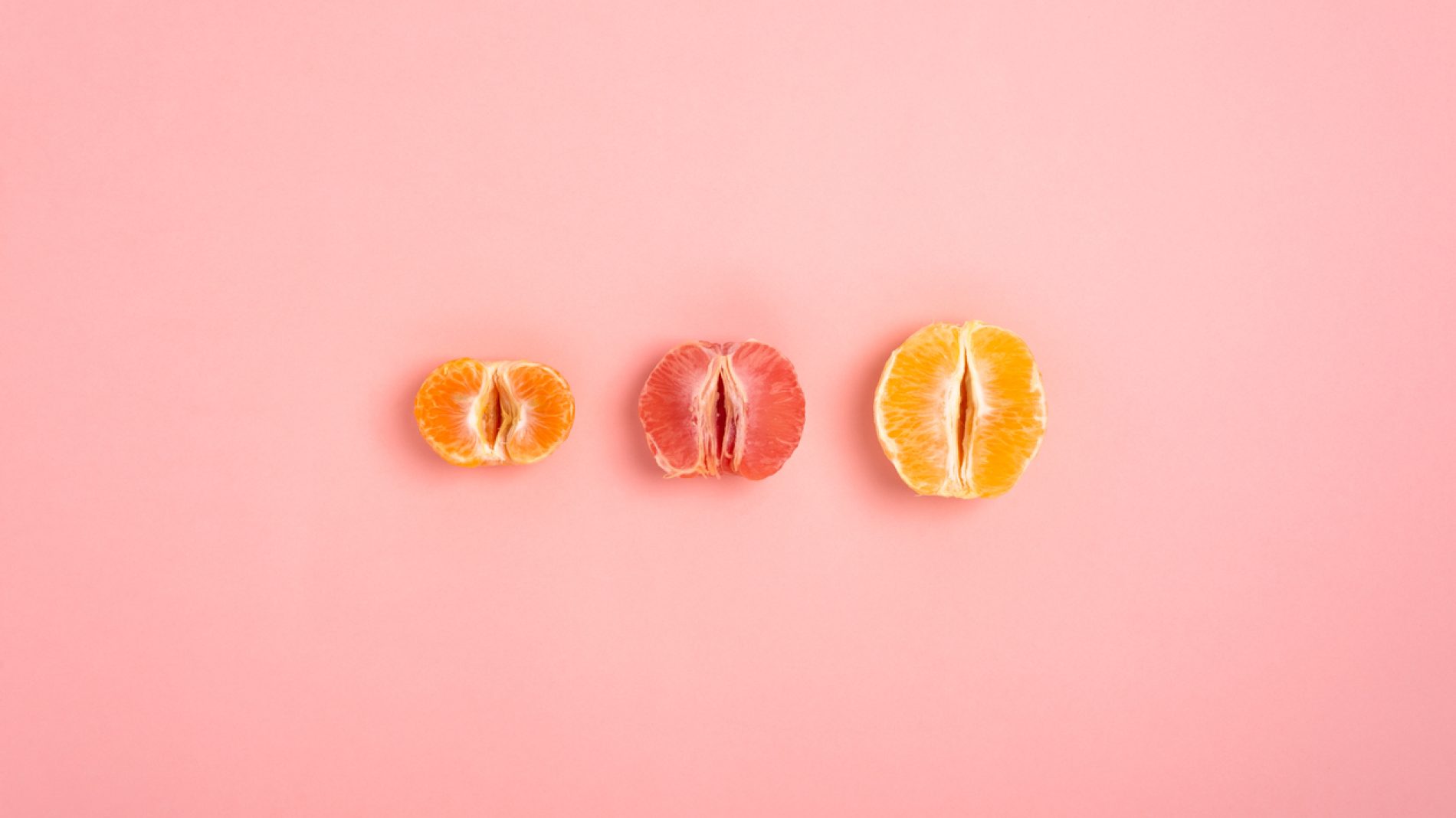 tangerine, grapefruit and orange cut in half on a peach background as a symbol of the vagina and female fertility, no people