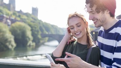 A happy young couple smiles as they relax outdoors by the river.