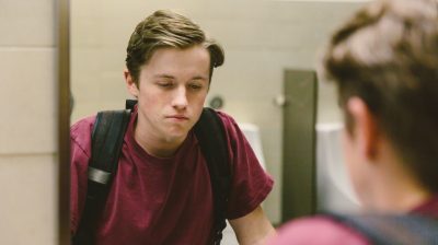 Depressed teen looks at himself in bathroom mirror