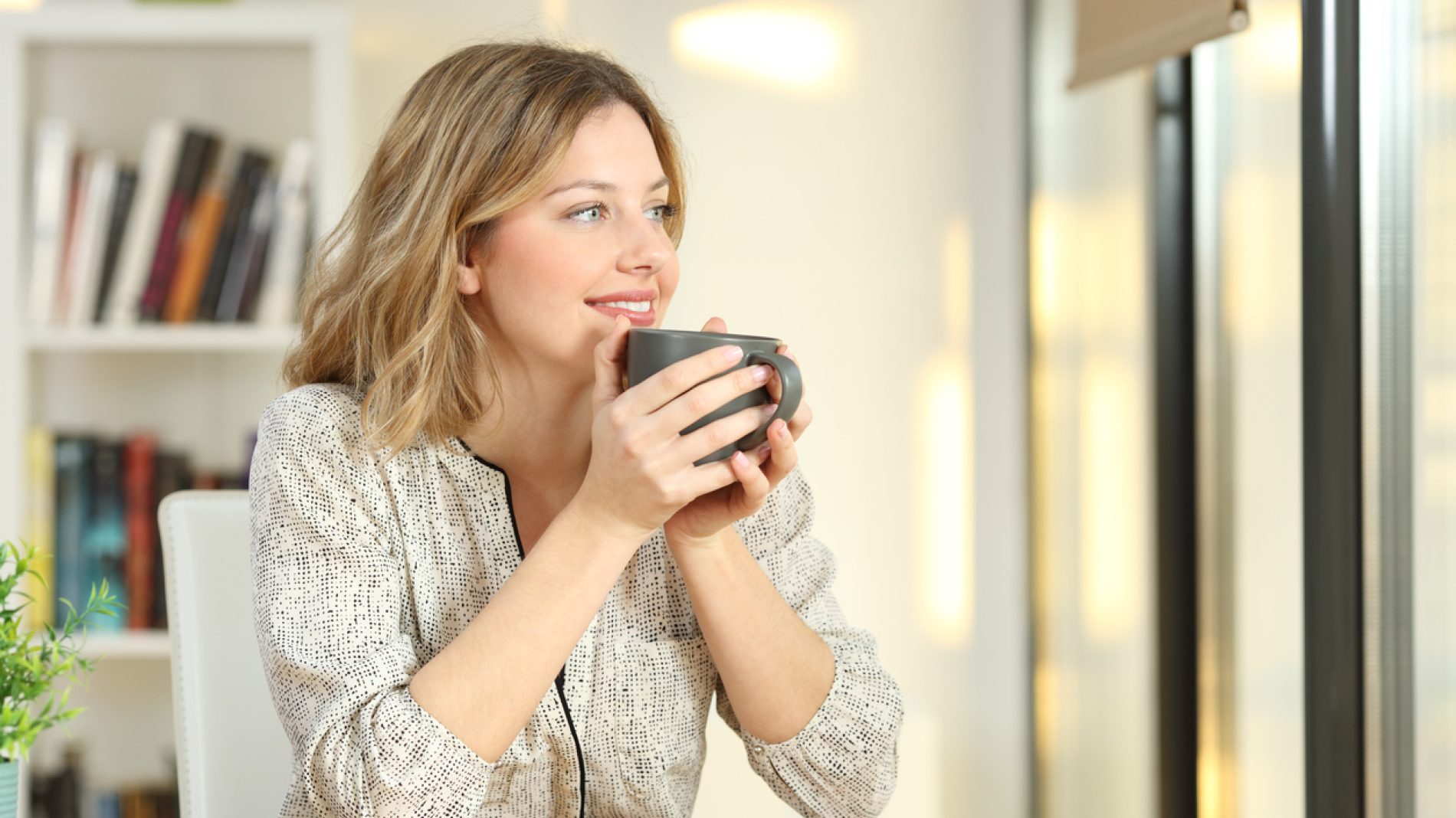 Woman looking through a window drinking coffee