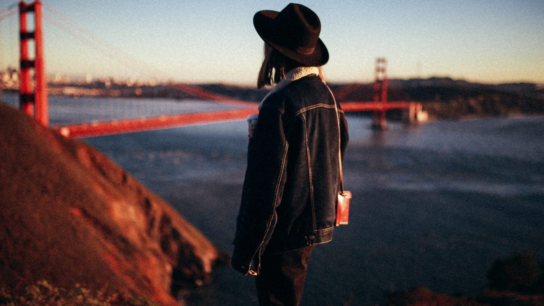 Photo of a person wearing a hat and staring at the Golden Gate Bridge in the distance