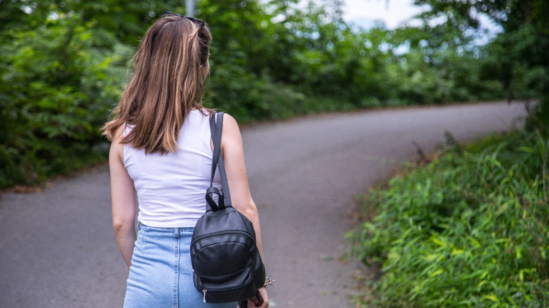 a feminine presenting person with a backpack walks along a path lined by shrubs
