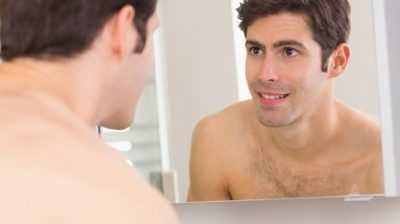 A shirtless man looking in the mirror