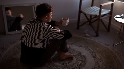 a masculine presenting person sits on a circular rug with their legs crossed holding a cup of tea mindfulness sixth year