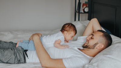 Photo of a person lying on a bed with a small baby resting on their chest