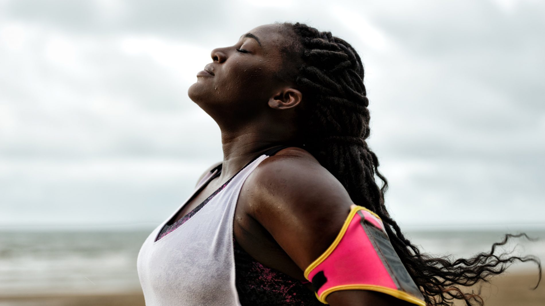 african woman standing under the rain,eyes closed, after workout on beach