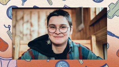 head and shoulders shot of non binary person with short hair and glasses smiling to camera