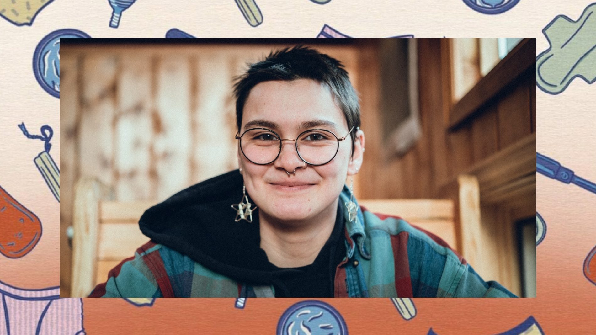head and shoulders shot of non binary person with short hair and glasses smiling to camera