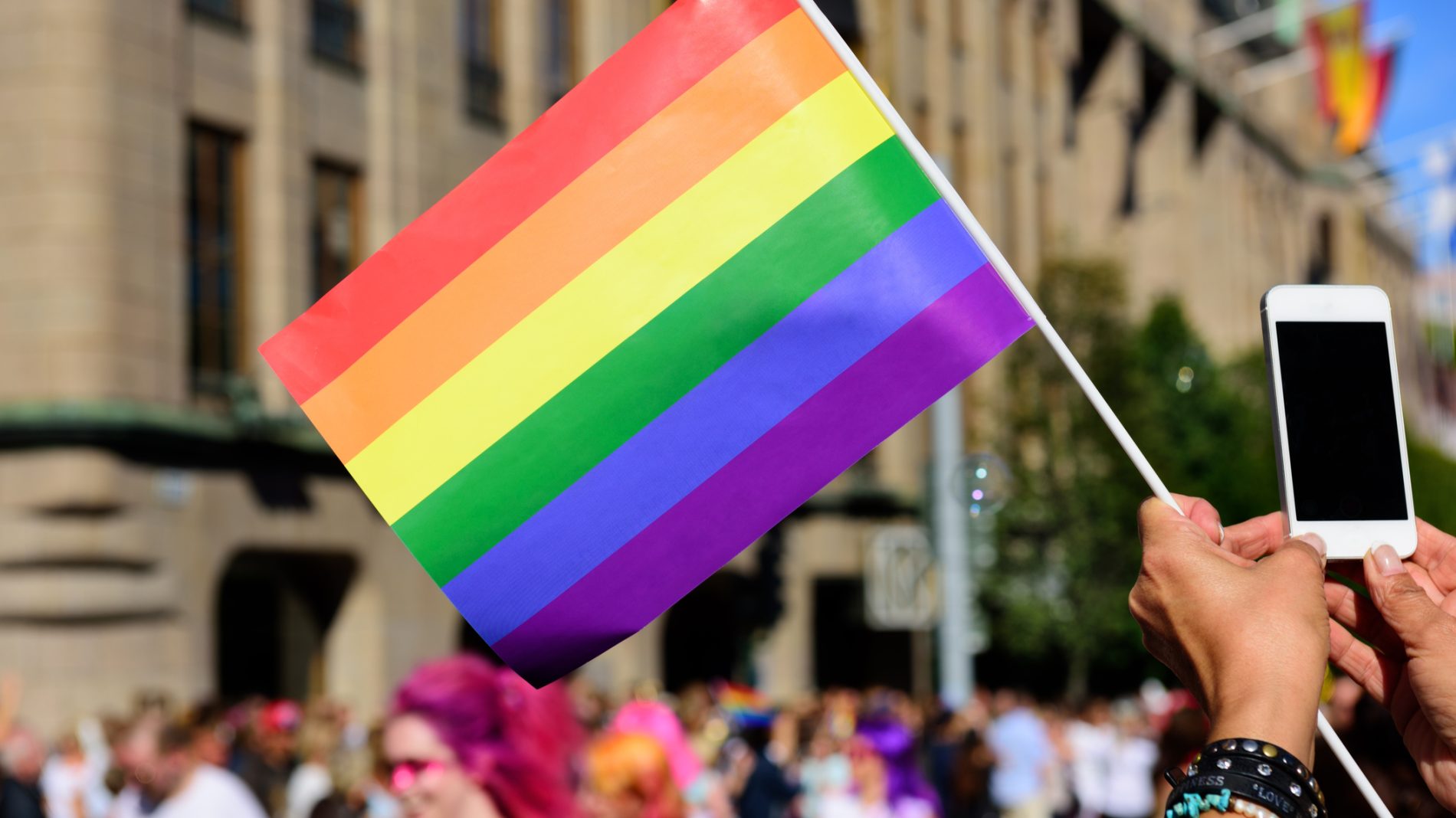 Someone holding pride colour flag with people in the background