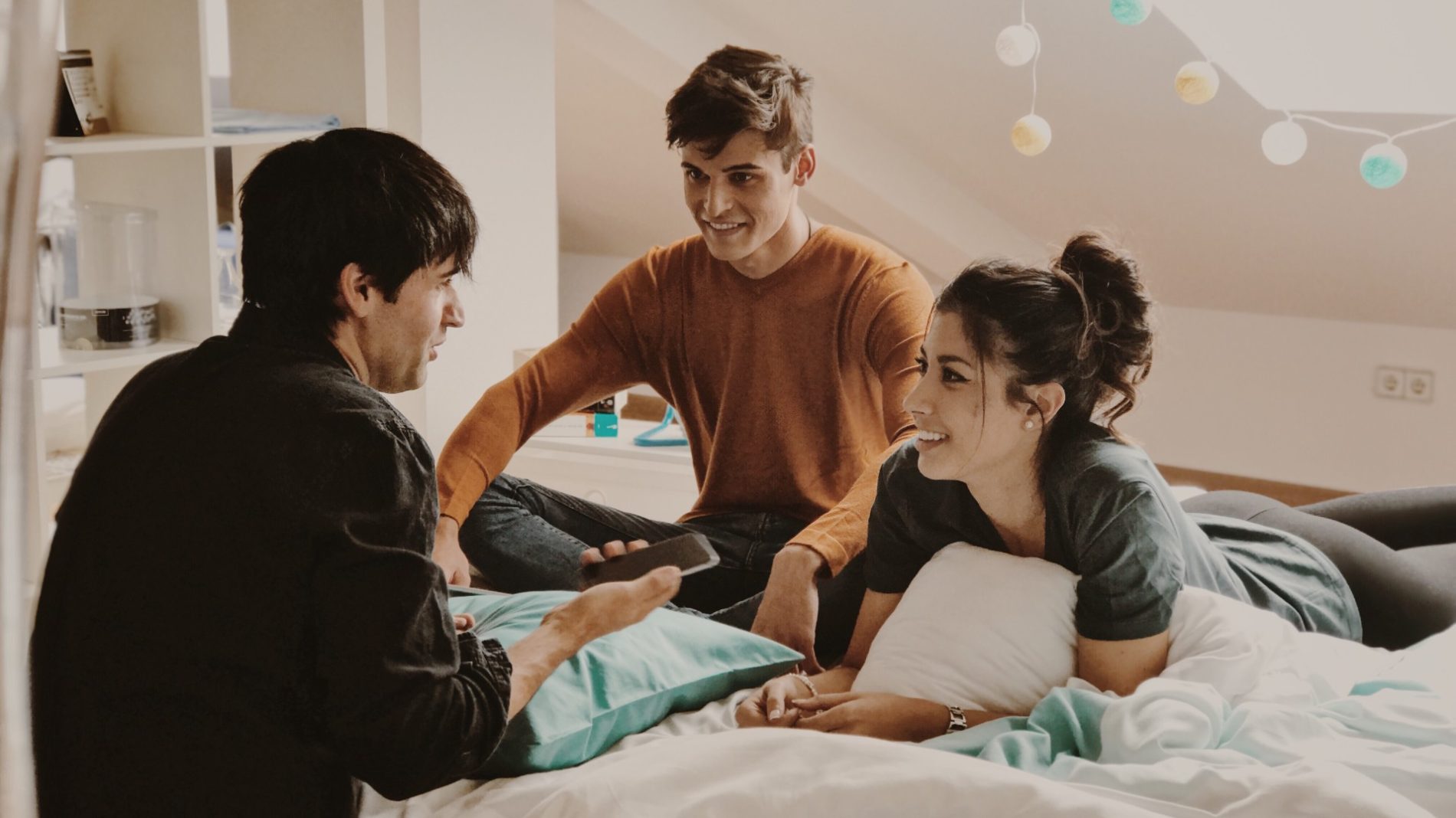 Photo of three young people sitting on a bed while talking