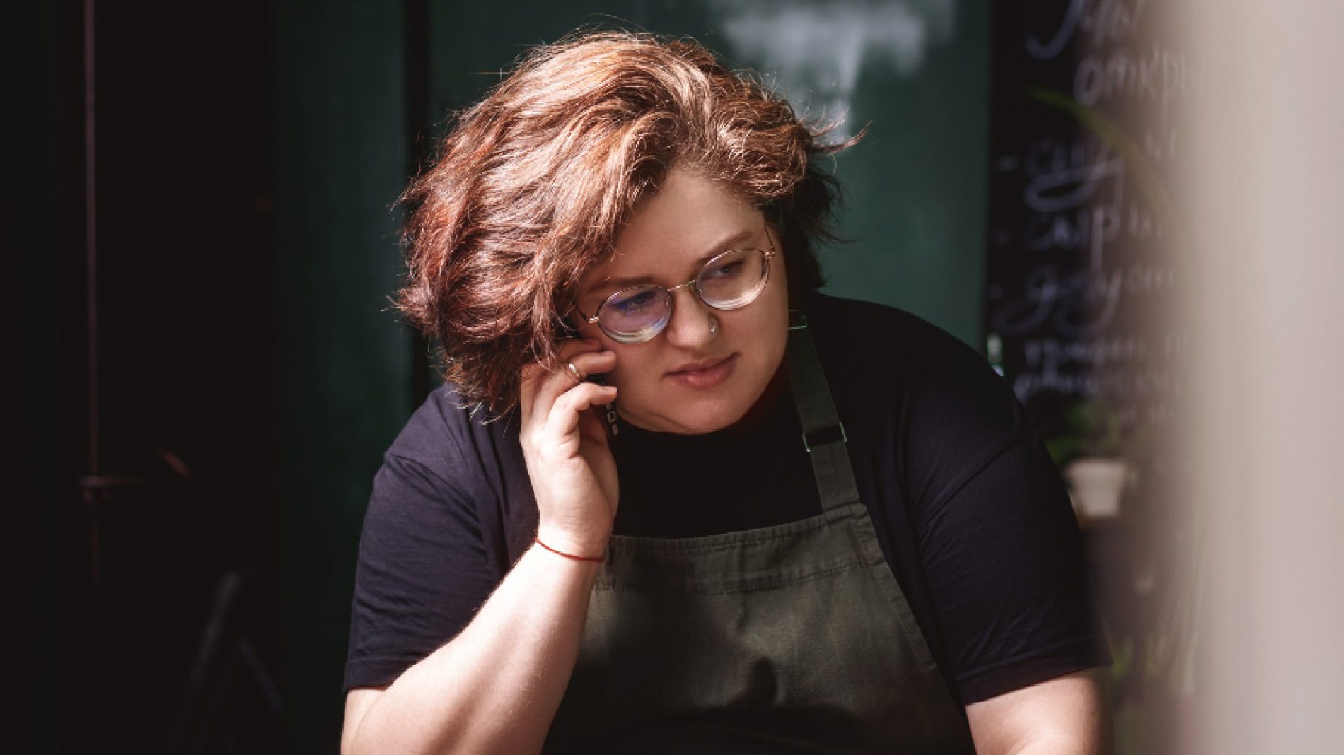 Young feminine person in glasses with short, curly hair wearing apron is on the phone. | quitting your job
