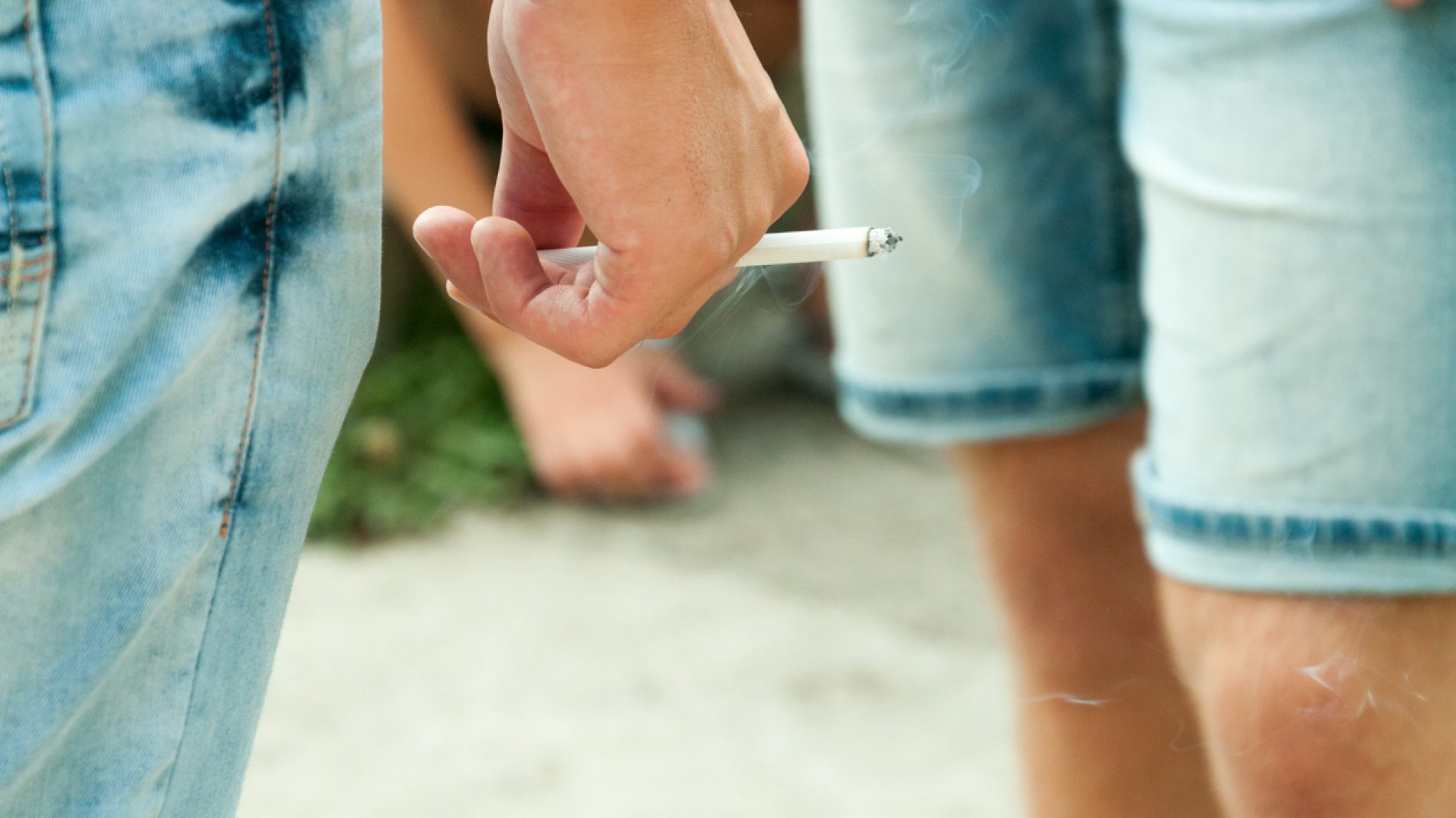 Hand of young man holding cigarette and standing in group of people on the street.