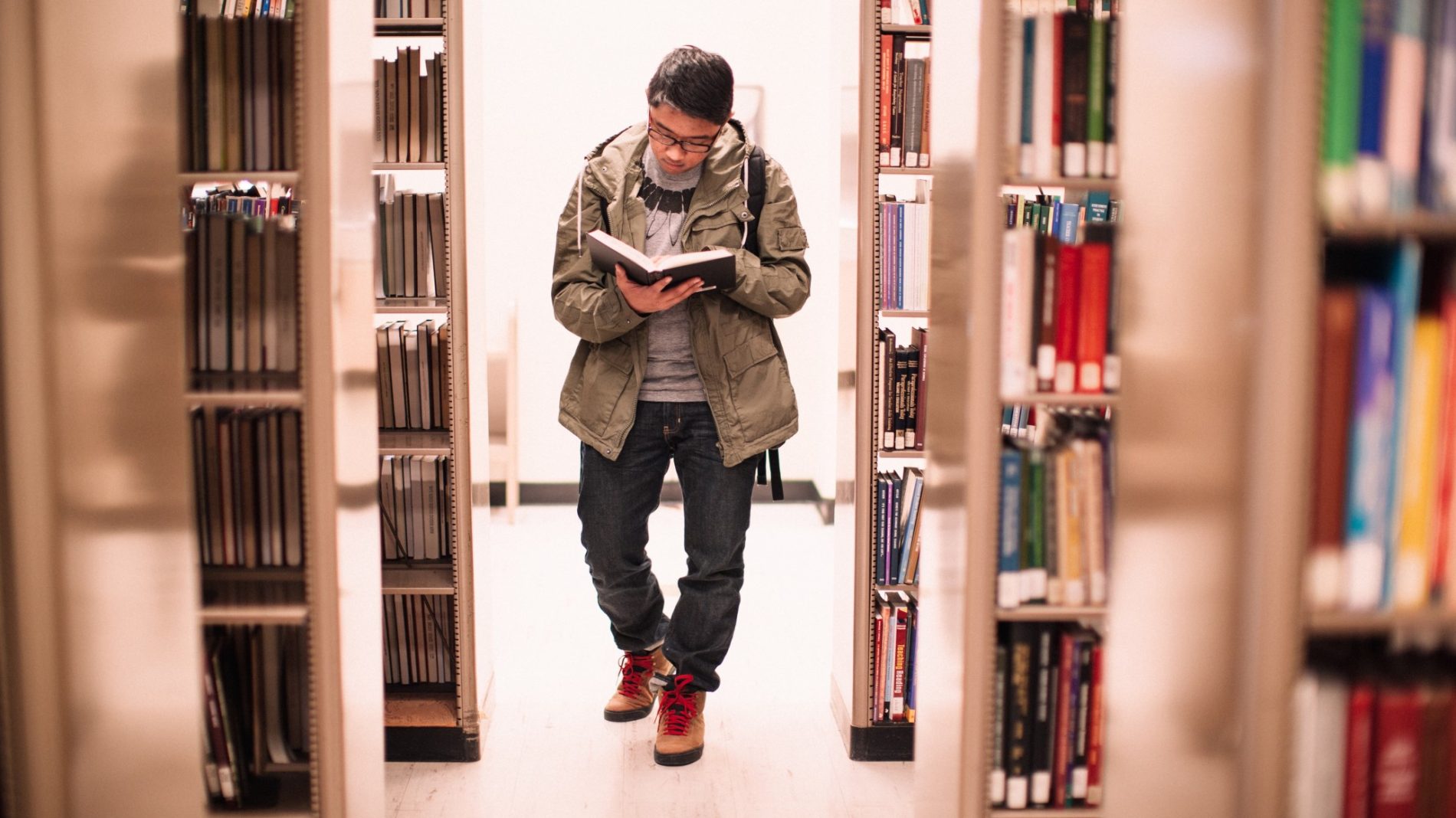 Photo of a person walking through a library while reading a book - student assistance fund