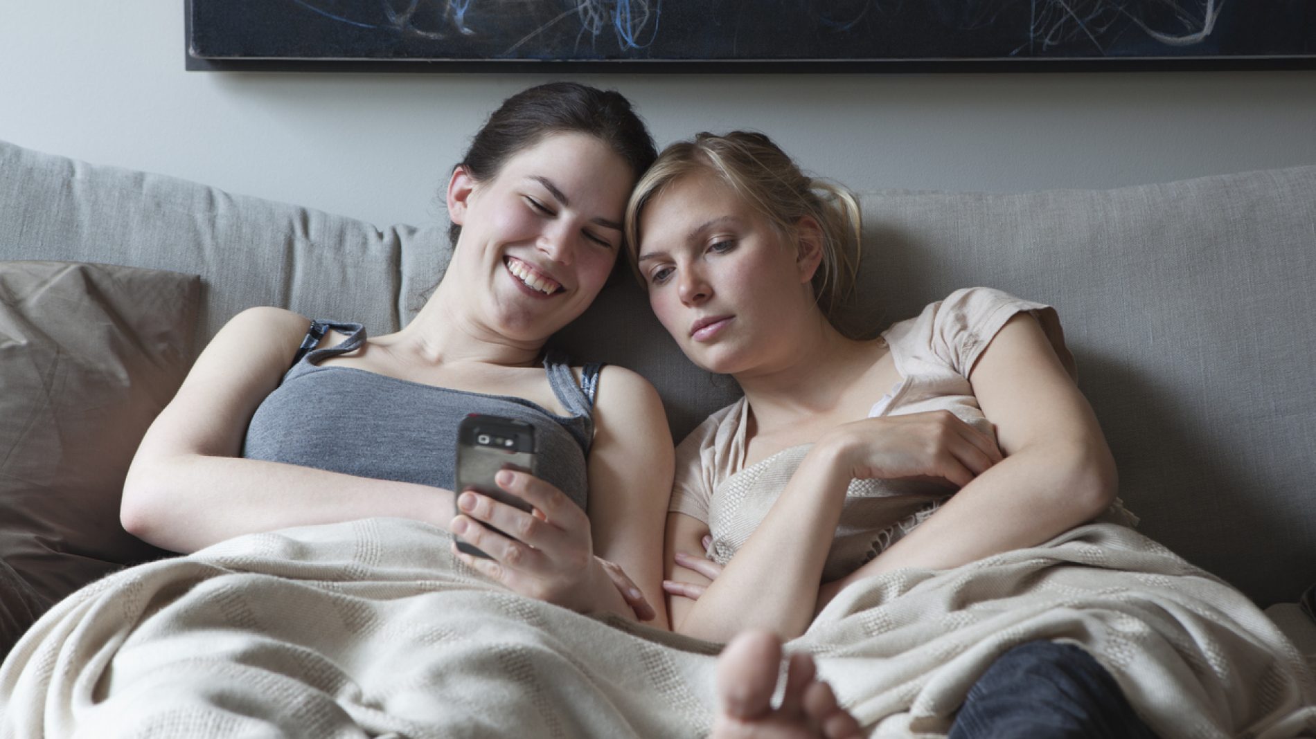 2 young women sit on a couch together looking at a phone