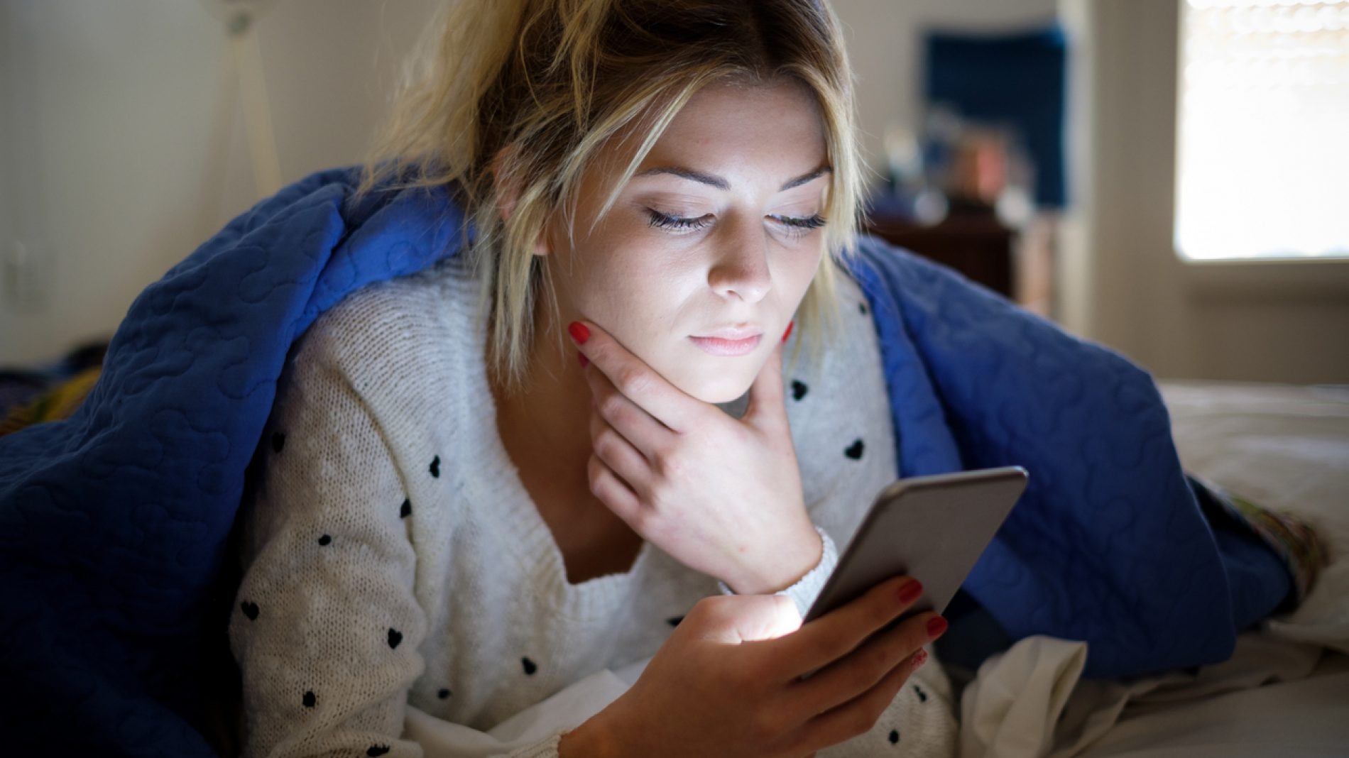 Disappointed sad woman holding mobile phone while laying on bed