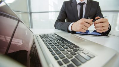 Close-up of laptop and businessman sitting at the table behind