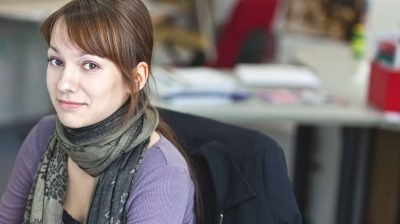 Photo of a young person sitting at a desk wearing a scarf